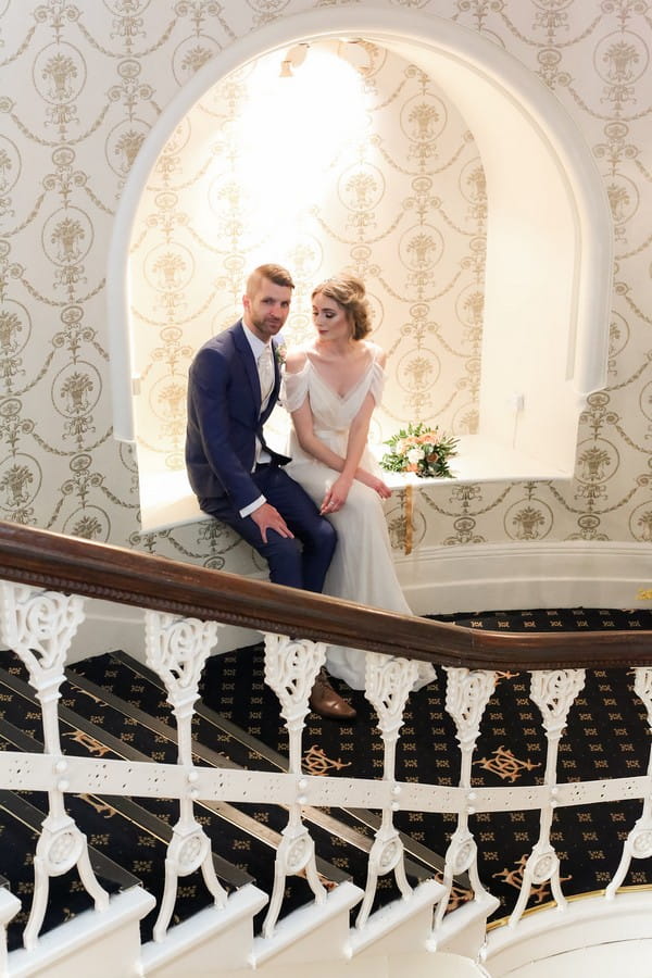 Bride and groom sitting in alcove by stairs of The Duke of Cornwall Hotel