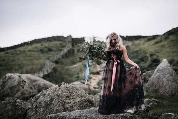 Bride wearing dark blue wedding dress walking over rocks in Lake District