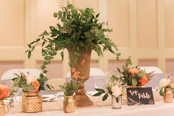 Urn of foliage with copper and gold votives of flowers on wedding table