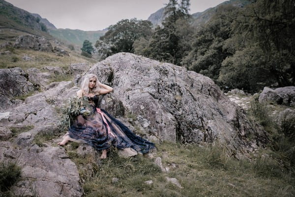 Bride sitting against rocks in Lake District