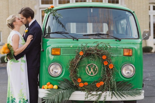 Bride and groom kissing by VW van with orange flower wreath and citrus fruits on the front