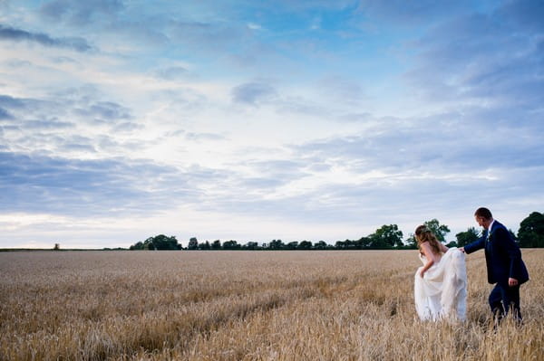 Bride and groom walking across wheat field