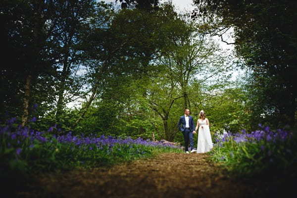 Bride and groom walking through woodland with bluebells