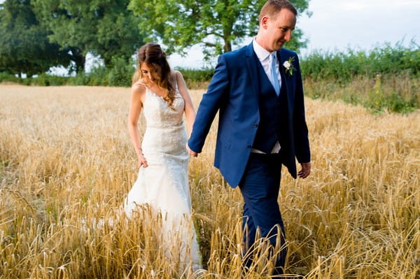 Bride and groom holding hands walking through wheat