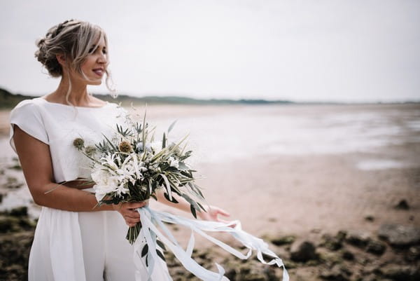 Bride holding bouquet on beach in Cumbria