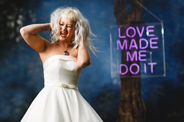 Rock n roll bride in front of neon sign which reads Love Made Me Do It