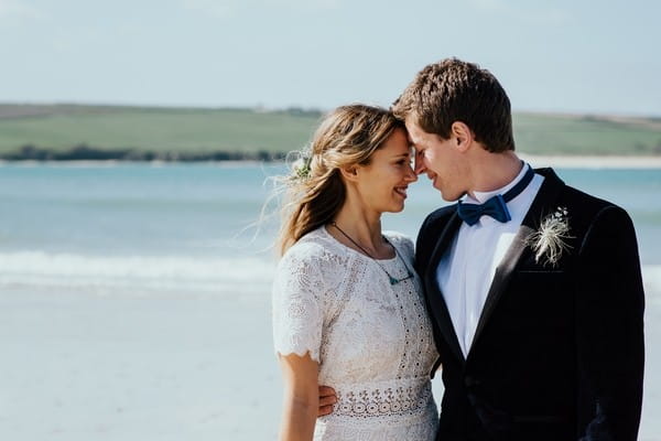 Bride and groom touching heads on beach