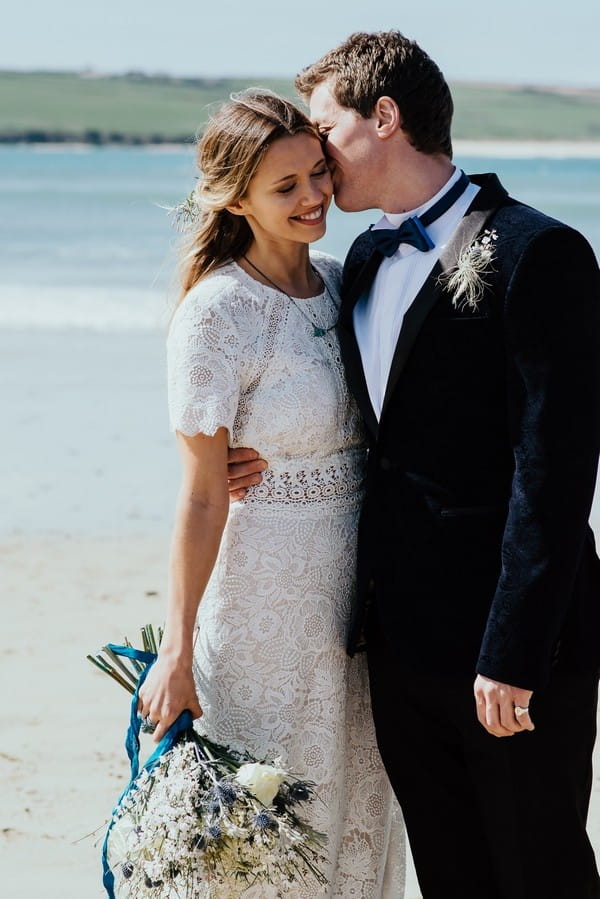 Groom kissing bride on cheek on beach