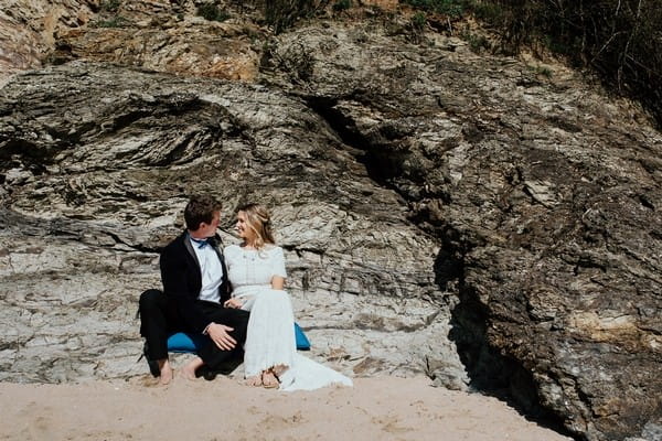 Bride and groom sitting by rocks on beach