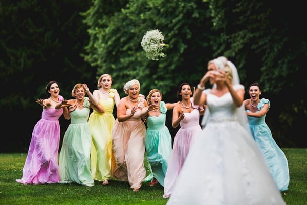 Bride throwing bouquet towards bridesmaids in colourful dresses - Picture by Aaron Storry Photography