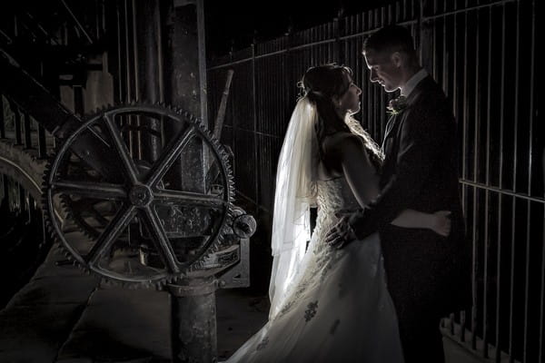 Bride and groom standing by large mechanical cog - Picture by Peter Anslow Photography