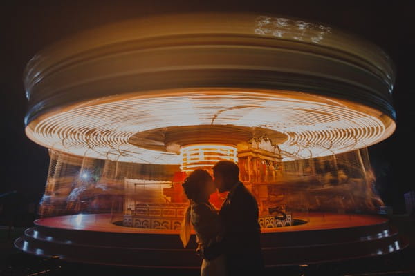 Bride and groom kissing in front of blurred fairgroung carousel - Picture by Rob Dodsworth Photography