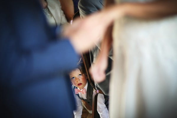 Pageboy looking out from under chair during wedding ceremony - Picture by Neale James