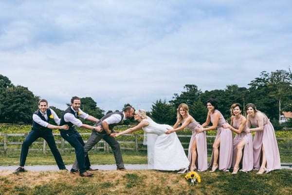 Bridesmaids and groomsmen holding bride and groom back as they kiss