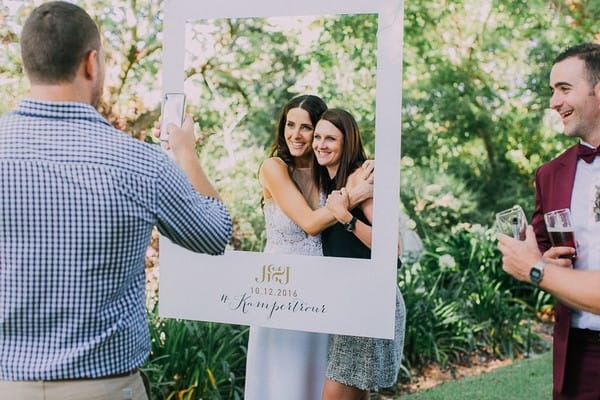 Bride and friend having picture taken behind personalised wedding frame