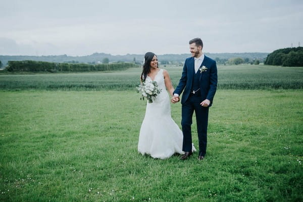 Bride and groom holding hands as they walk across field