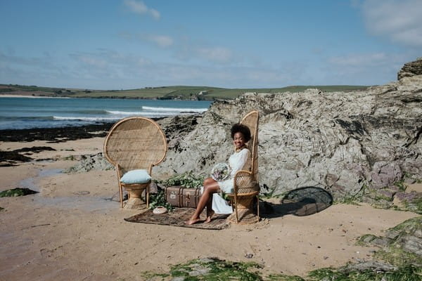 Bride sitting on chair by rocks on beach