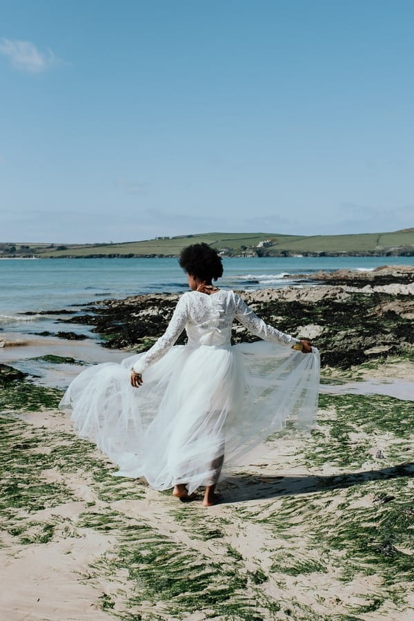 Bride holding out skirt as she walks on beach