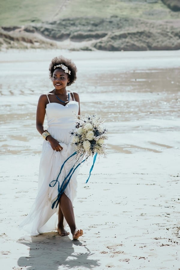 Bride walking on beach carrying bouquet