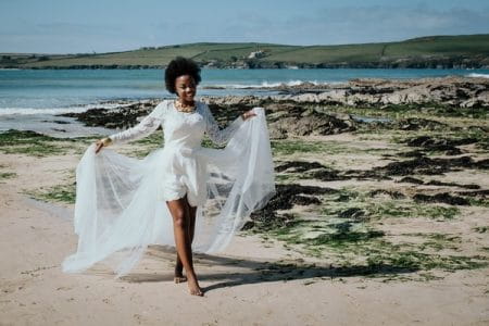 Bride holding out skirt of wedding dress as she walks on the beach