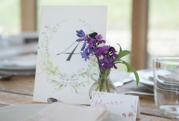 Small vase of purple flowers next to table number