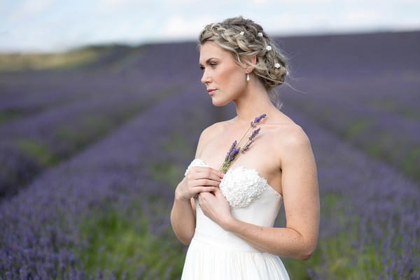 Bride holding sprig of lavender to her chest while standing in a lavender field - Picture by Eva Tarnok Photography