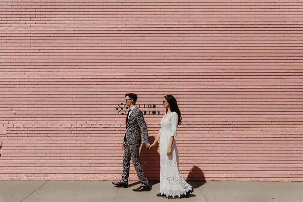 Cool bride and groom walking next to pink wall - Picture by The Hendrys Photography