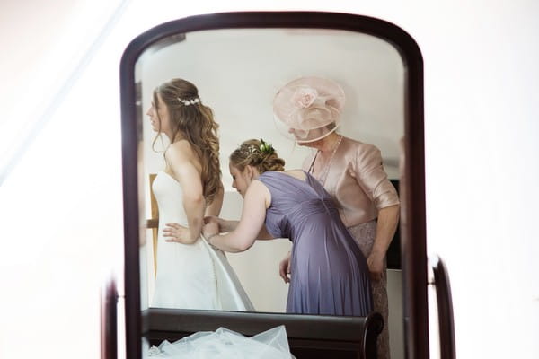 Reflection in mirror of bridesmaid doing up back of bride's wedding dress