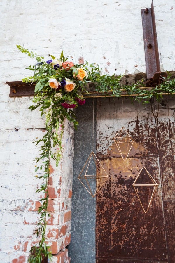Flower and foliage arrangement over door with hanging geometric shapes