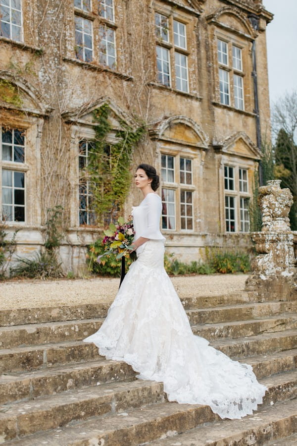 Bride with dress train trailing down steps outside Brympton House