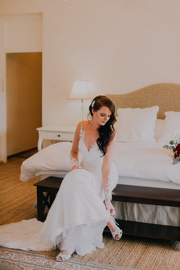 Bride sitting on bed putting shoes on