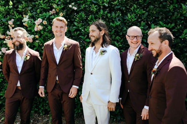 Groom in white suit with groomsmen in burgundy suits