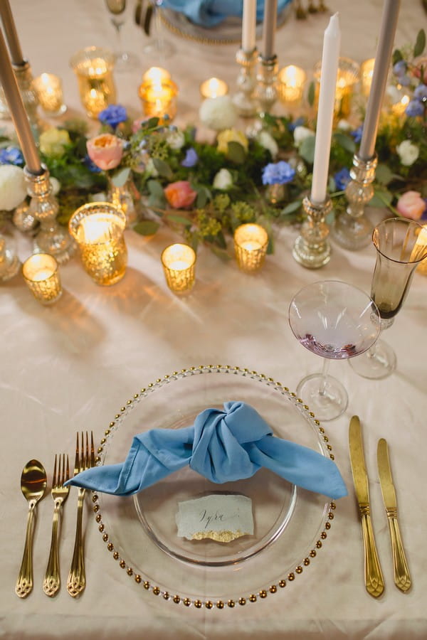 Wedding place setting with gold cutlery and blue napkin