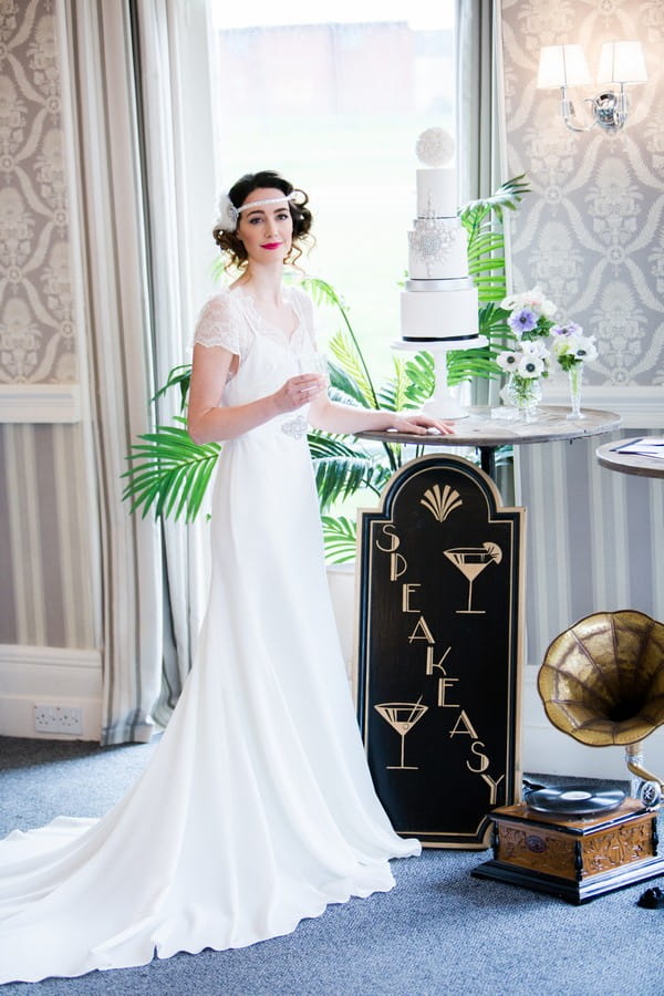 1920s bride holding drink standing next to wedding cake