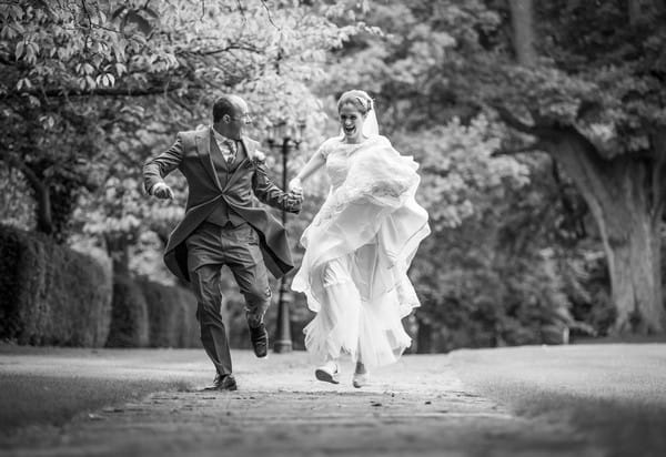 Bride and groom running down a path holding hands - Picture by Peter Rollings Photography