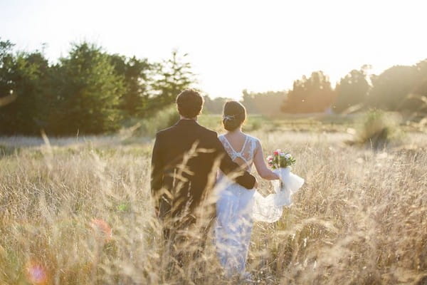 Back view of bride and groom walking though a field of wheat - Picture by Dos Clavos