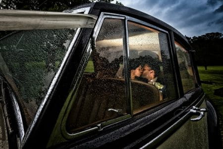 Bride and groom kissing in back of wedding car in the rain - Picture by Photography By Soven