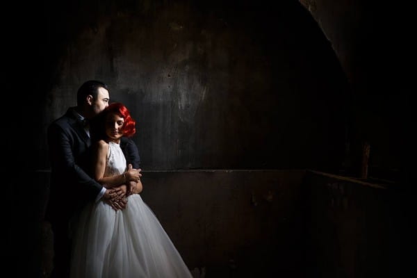 Groom hugging bride from behind in dark room - Picture by Marius Tudor Photography