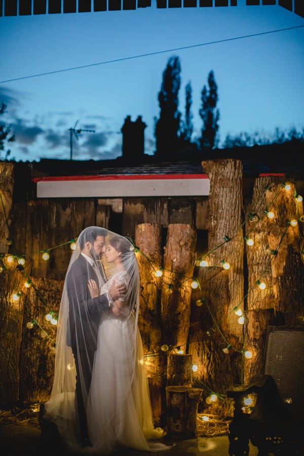 Bride and groom by logs covered in lights