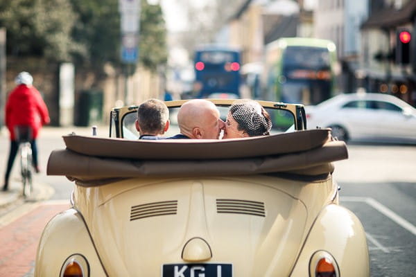 Bride and groom kissing in back of convertible VW Beetle wedding car