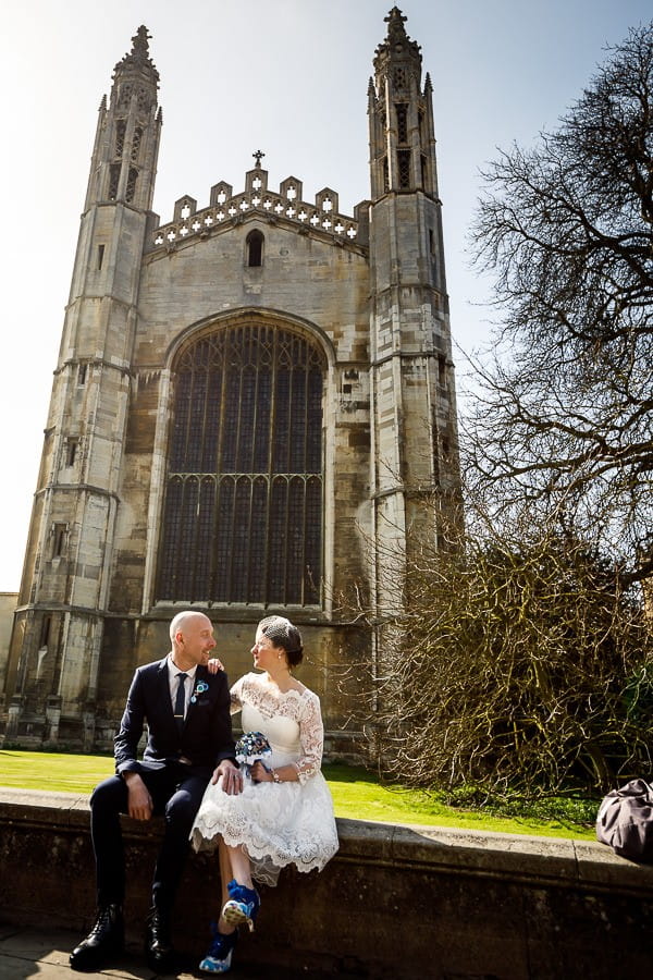 Bride and groom sitting on wall outside Cambridge Cathedral