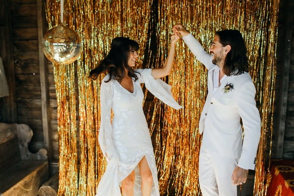Bride and groom in front of gold sparkly backdrop with disco ball