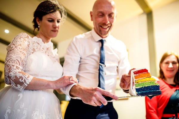 Bride and groom cutting rainbow wedding cake