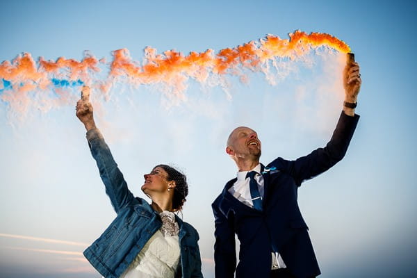 Bride and groom waving orange smoke bombs