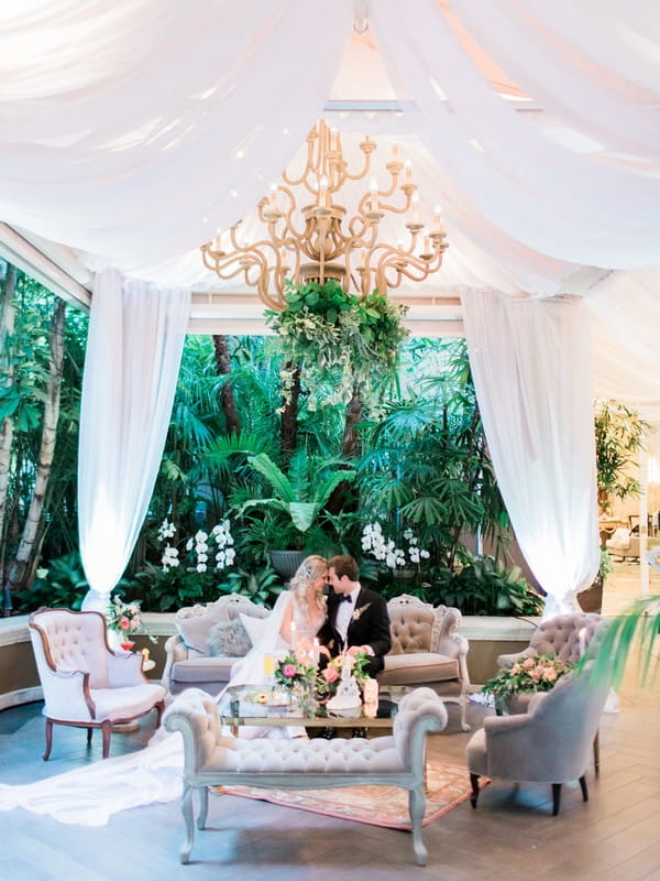 Bride and groom sitting n couch below chandelier