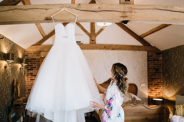 Bride looking at wedding dress hanging from beam