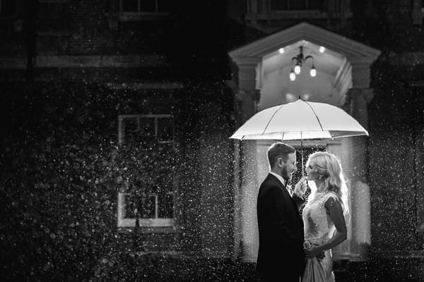 Black and white picture of bride and groom under umbrella in the rain - Picture by Photography by Suzanne Fossey