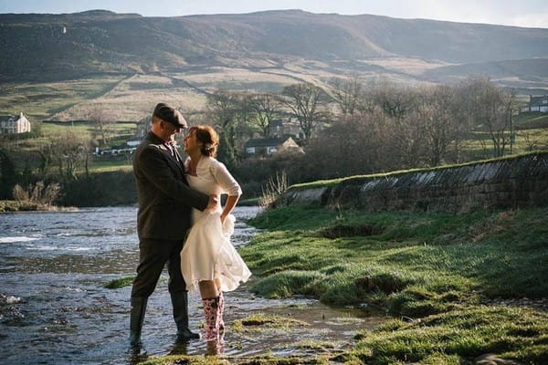 Bride and groom in wellies standing in stream in countryside - Picture by Emma and Rich