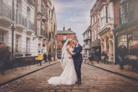 Bride and groom on cobbled street in Lincoln with blurred people walking past - Picture by AWPhotographic