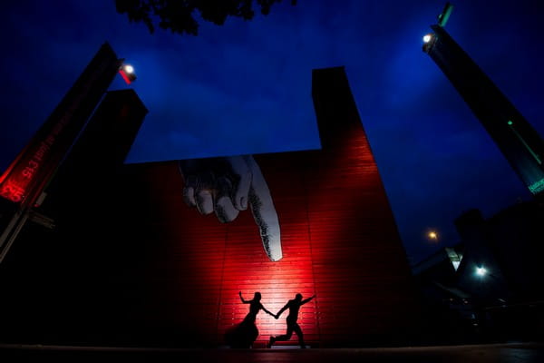 Silhouette of bride and groom running with graffiti finger pointing down at them - Picture by Alex Beckett Photography